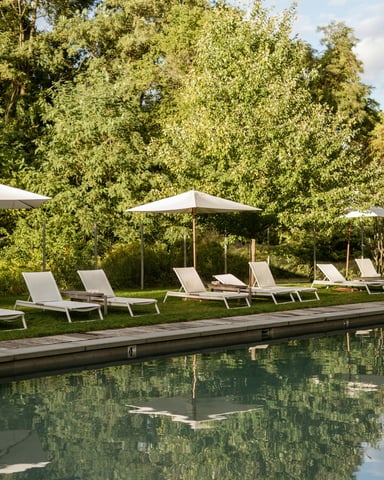 Pool lounge chairs and umbrellas reflected in still water