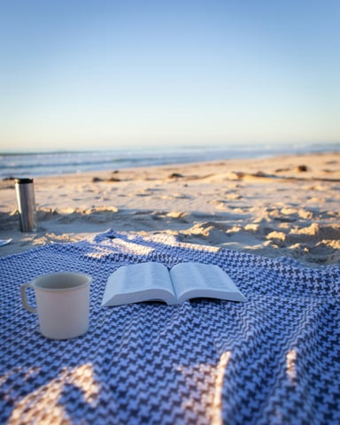 Open book and coffee mug on a beach blanket at sunrise