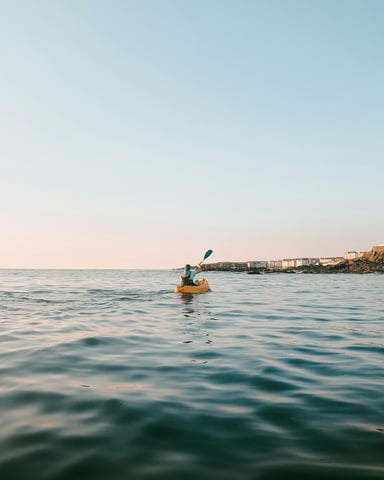 Solo kayaker paddling along a calm coastline at dusk
