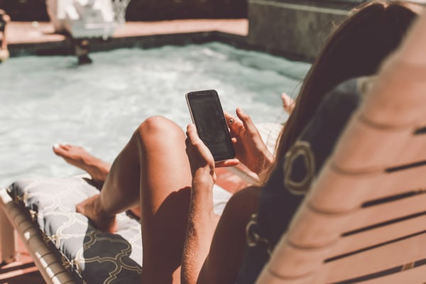 Person on a sun lounger by the pool checking their phone