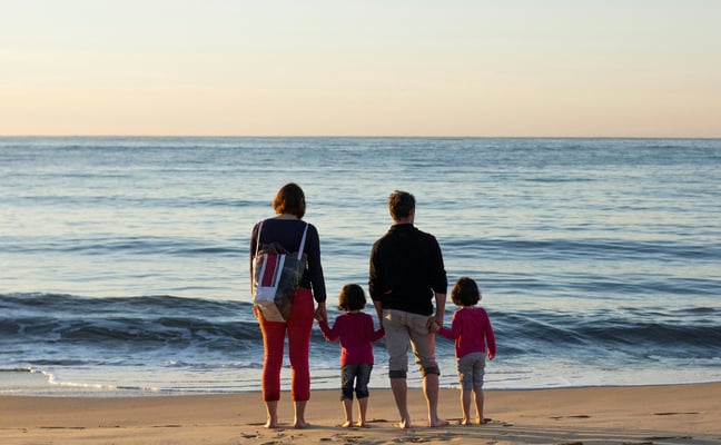 Family of four standing at the shoreline looking out to sea at dusk