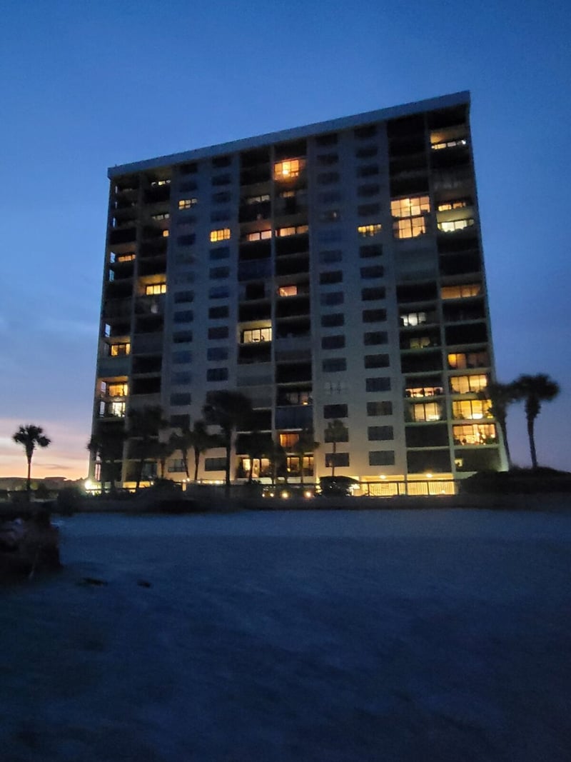 Multi-story beachfront condominium building at dusk with lit windows and palm trees nearby