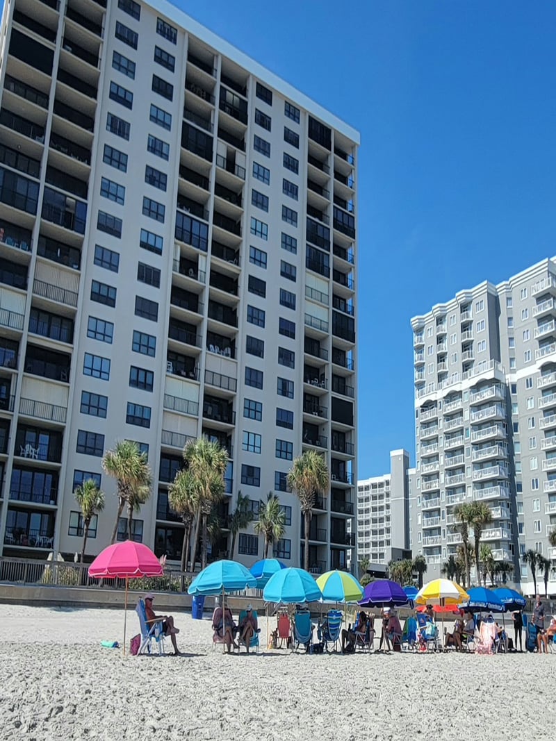 Beachfront high-rise condominiums with colorful umbrellas and beachgoers on sandy shore
