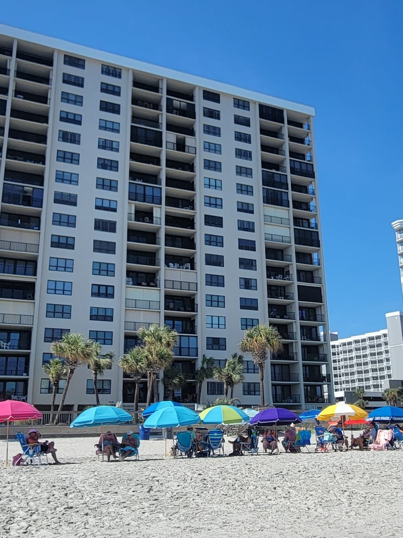 Beachfront apartment building with colorful umbrellas and beachgoers on sand below