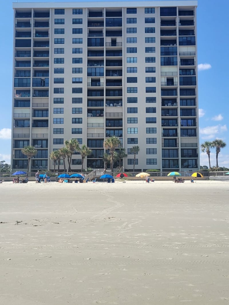 Multi-story beachfront condominium building with sandy beach and colorful umbrellas in foreground