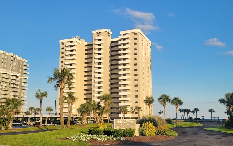 Beachfront condominium complex with multiple yellow high-rise towers, palm trees, and manicured lawns under clear blue sky