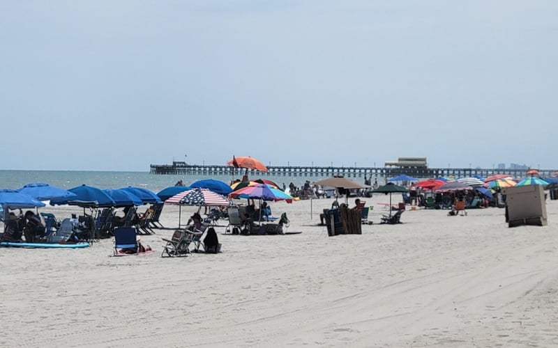 Crowded sandy beach with colorful umbrellas, beachgoers, and a pier in the distance