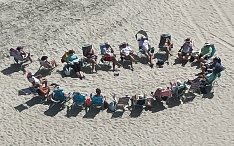 Aerial view of group of people sitting in circle on sandy beach with blue raft nearby